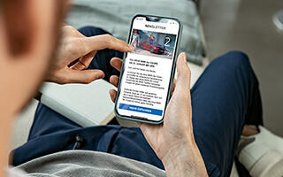 Mann liest auf einem Smartphone einen BMW-Newsletter mit Bild eines roten Sportwagens.