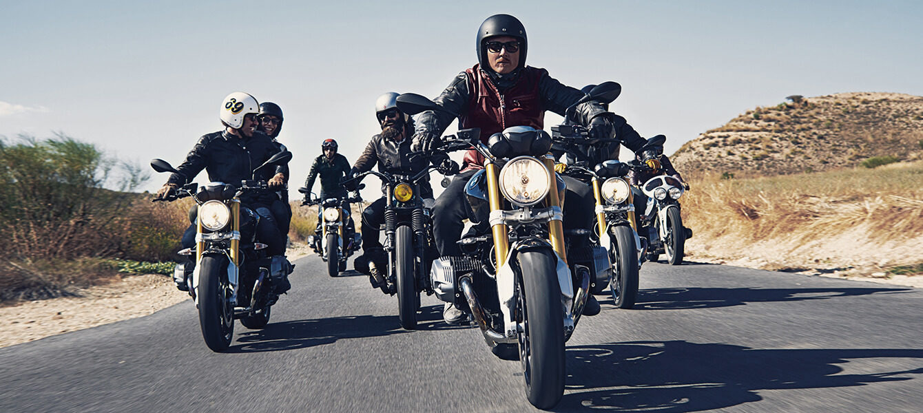Gruppe von BMW Motorradfahrern auf einer Landstraße, angeführt von mehreren BMW R nineT Modellen.