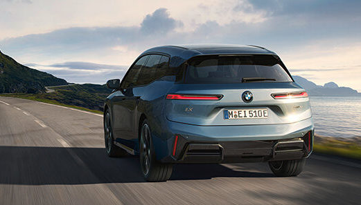 Der BMW iX fährt dynamisch über eine Küstenstraße mit Ausblick auf das Meer.