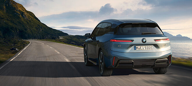 Der BMW iX fährt dynamisch über eine Küstenstraße mit Ausblick auf das Meer.