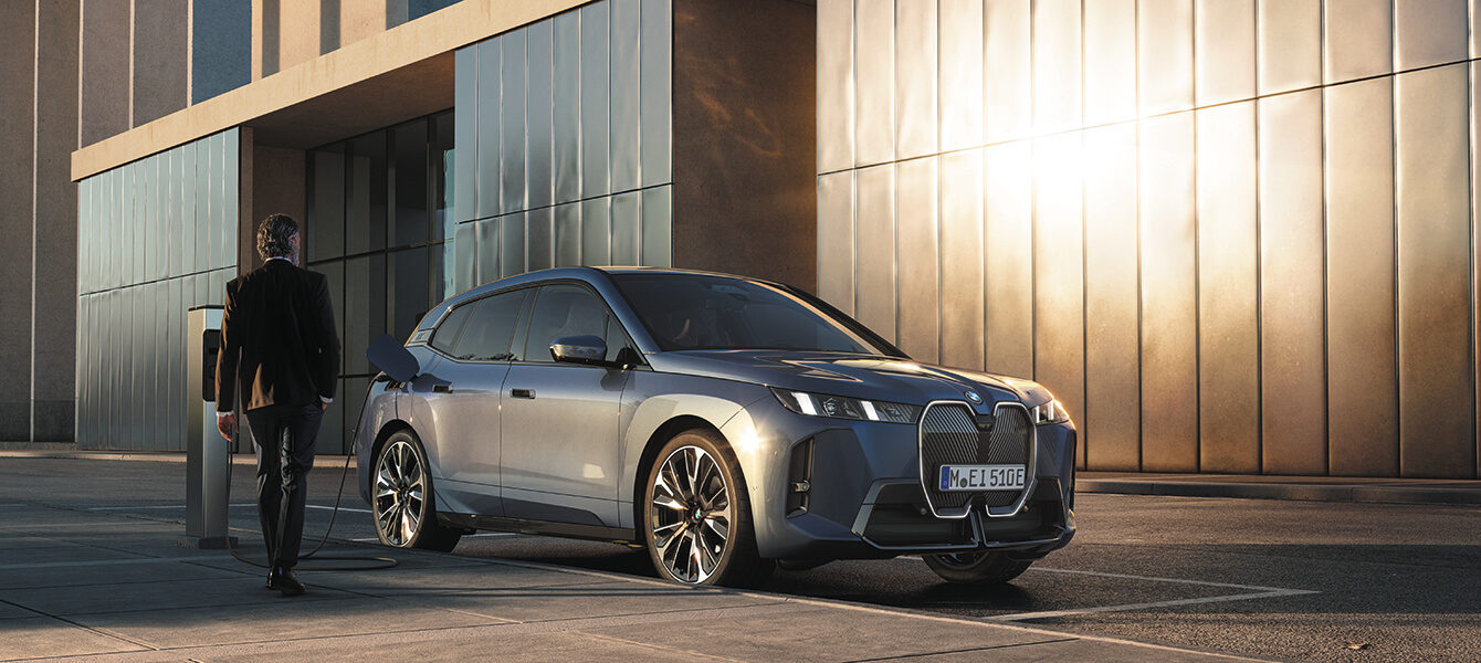 BMW iX wird an einer Ladestation in urbaner Umgebung geladen.
