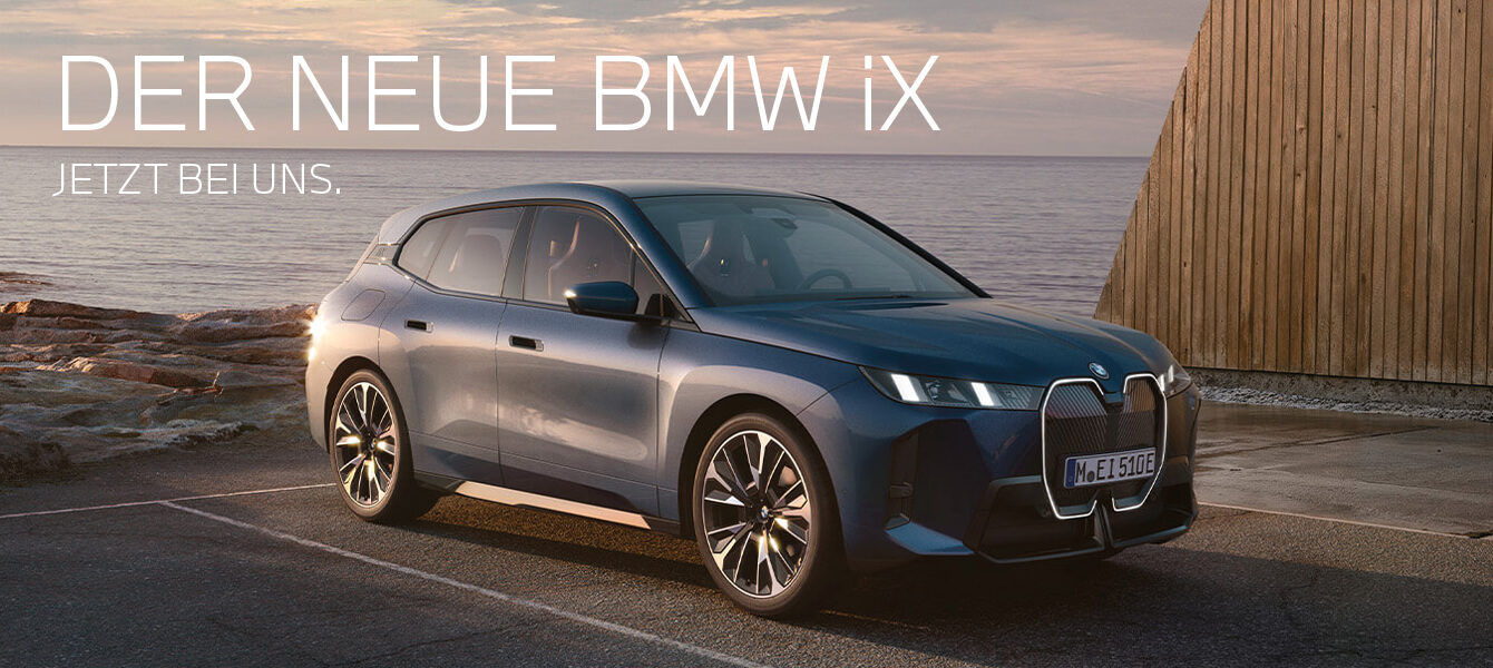 Der neue BMW iX in dunkelblauer Lackierung, geparkt vor einer modernen Küstenkulisse mit Holzarchitektur und Meerblick.
