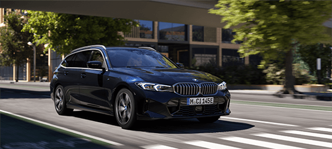 BMW 3er Touring Plug-in-Hybrid in dunkler Lackierung fährt dynamisch durch die Stadt bei Tageslicht.