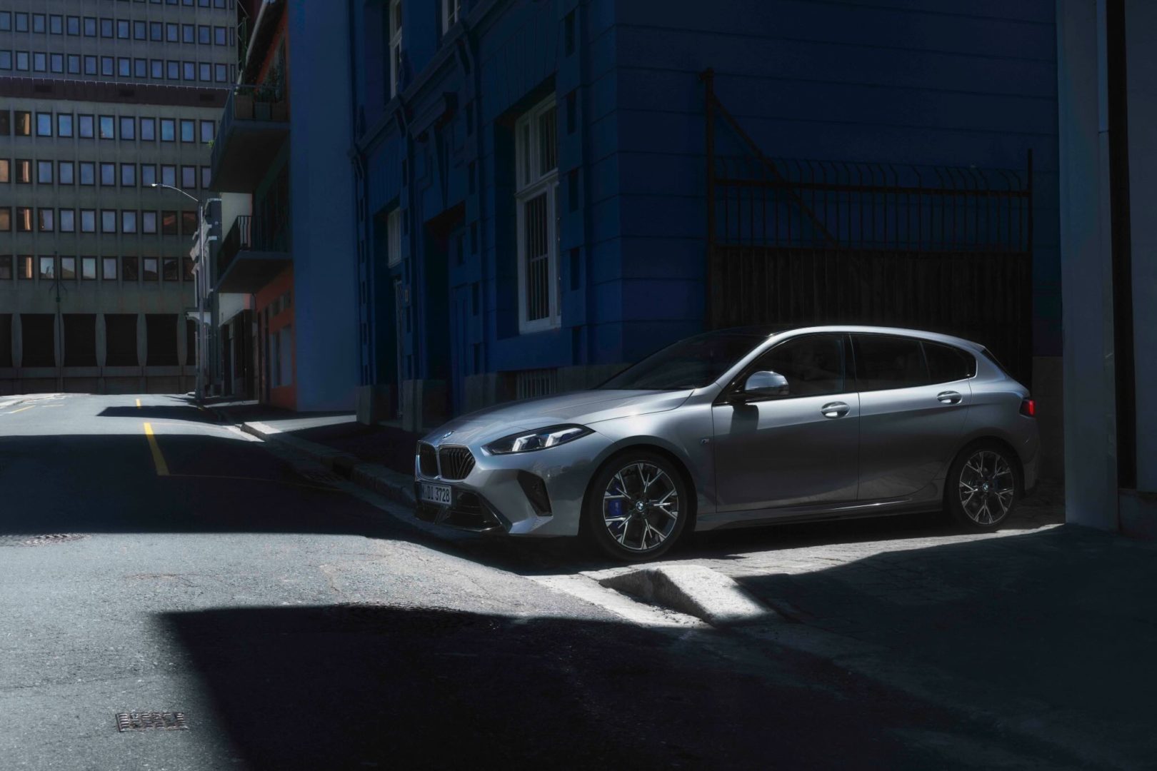 Ein silberner BMW 1er parkt in einer schattigen Seitengasse vor einem blauen Gebäude – aufgenommen. Erleben Sie ihn jetzt beim Autohaus Kühnert