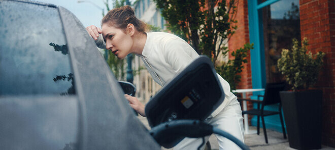Frau lädt ein Elektroauto an einer öffentlichen Ladesäule in der Stadt.