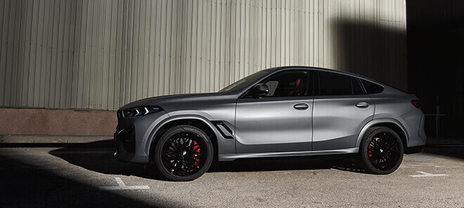 BMW X6 M Competition in Seitenansicht vor Industriegebäude.