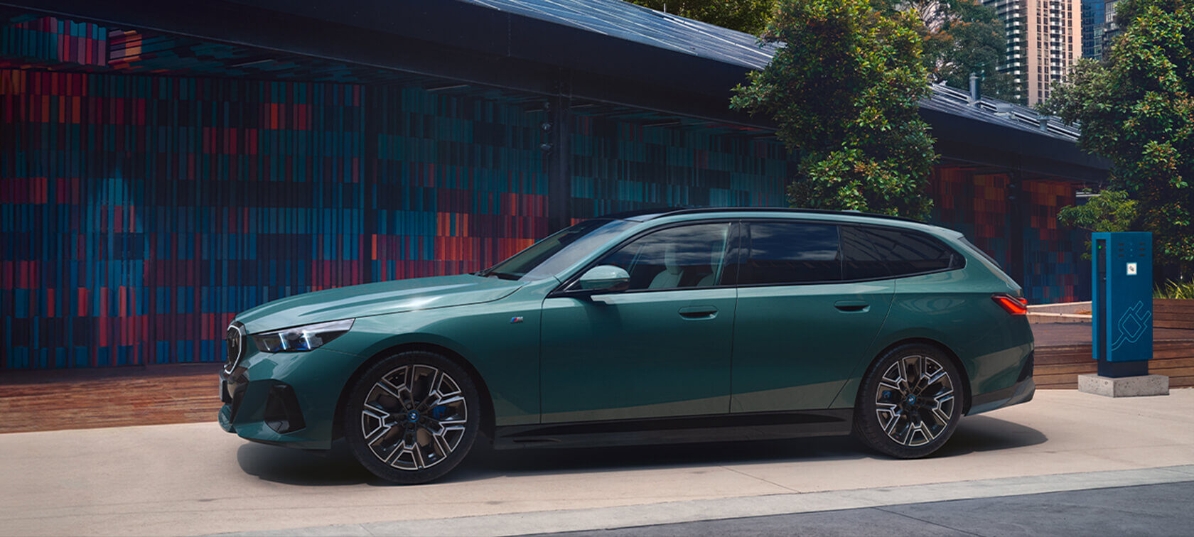 BMW i5 Touring in Grün an einer Ladestation – vollelektrischer BMW Kombi in urbaner Umgebung